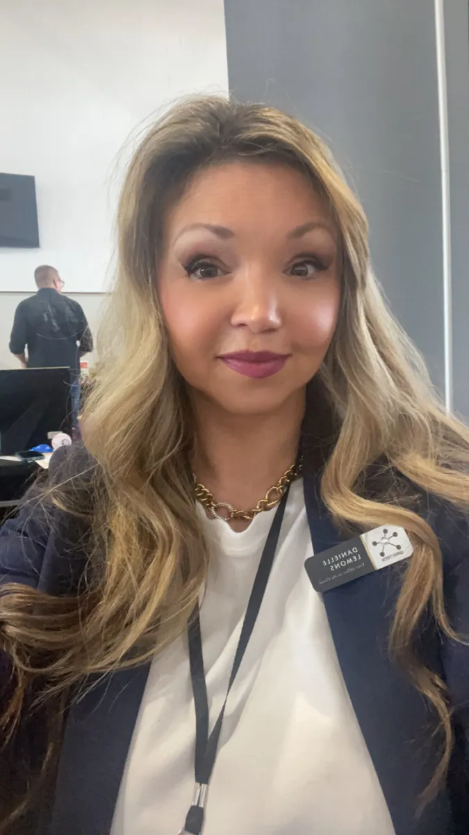 Danielle Lemons at the office with name badge. Danielle Lemons, Vice President of Operations at DirecTech Connect, at the office in a navy jacket and name badge.