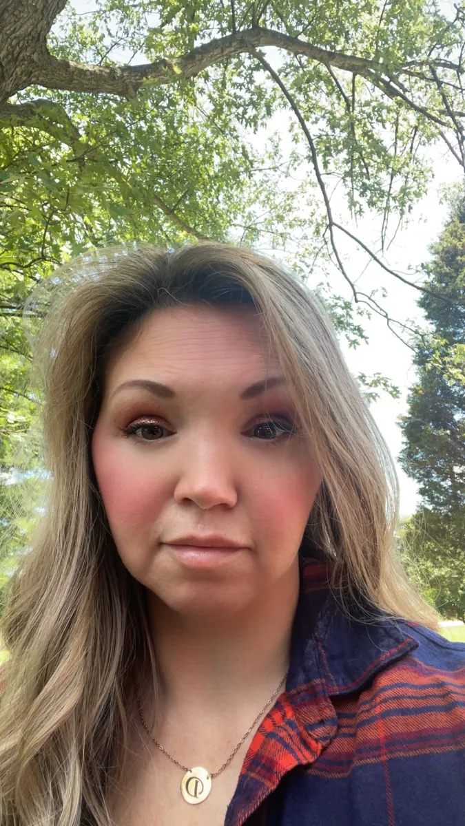 Danielle Lemons outdoors in a plaid shirt. Danielle Lemons, Vice President of Operations at DirecTech Connect, outdoors under the trees in a plaid shirt.
