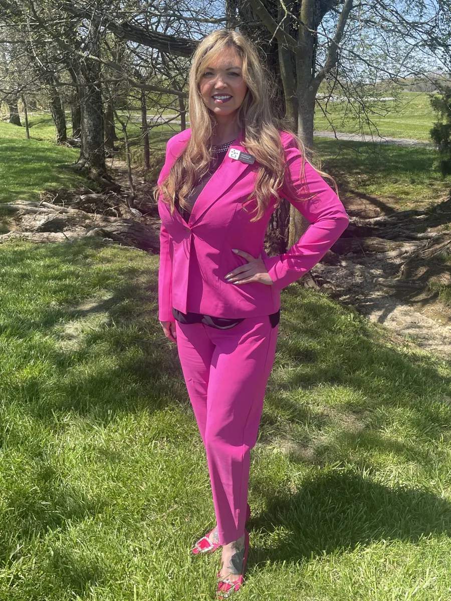 Danielle Lemons in a pink suit, full length. Danielle Lemons, Vice President of Operations at DirecTech Connect, in a pink suit, shown full length outdoors.