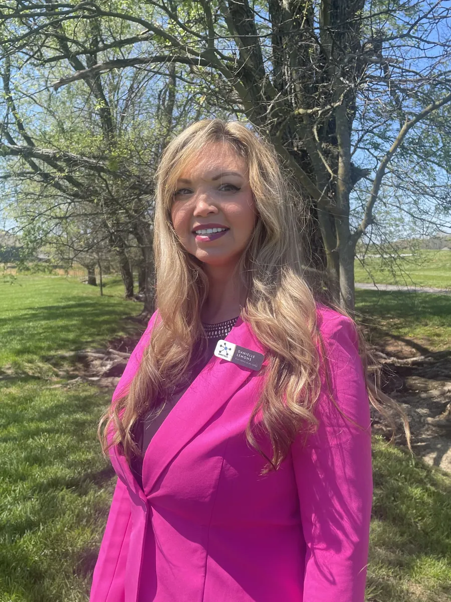 Danielle Lemons in a pink suit, outdoor portrait. Danielle Lemons, Vice President of Operations at DirecTech Connect, in a pink suit outdoors.