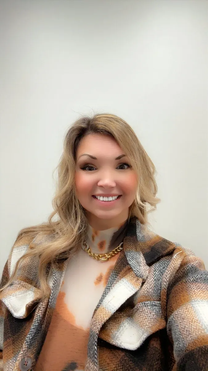 Danielle Lemons in a plaid plaid jacket. Danielle Lemons, Vice President of Operations at DirecTech Connect, smiling in a plaid plaid jacket and gold chain.